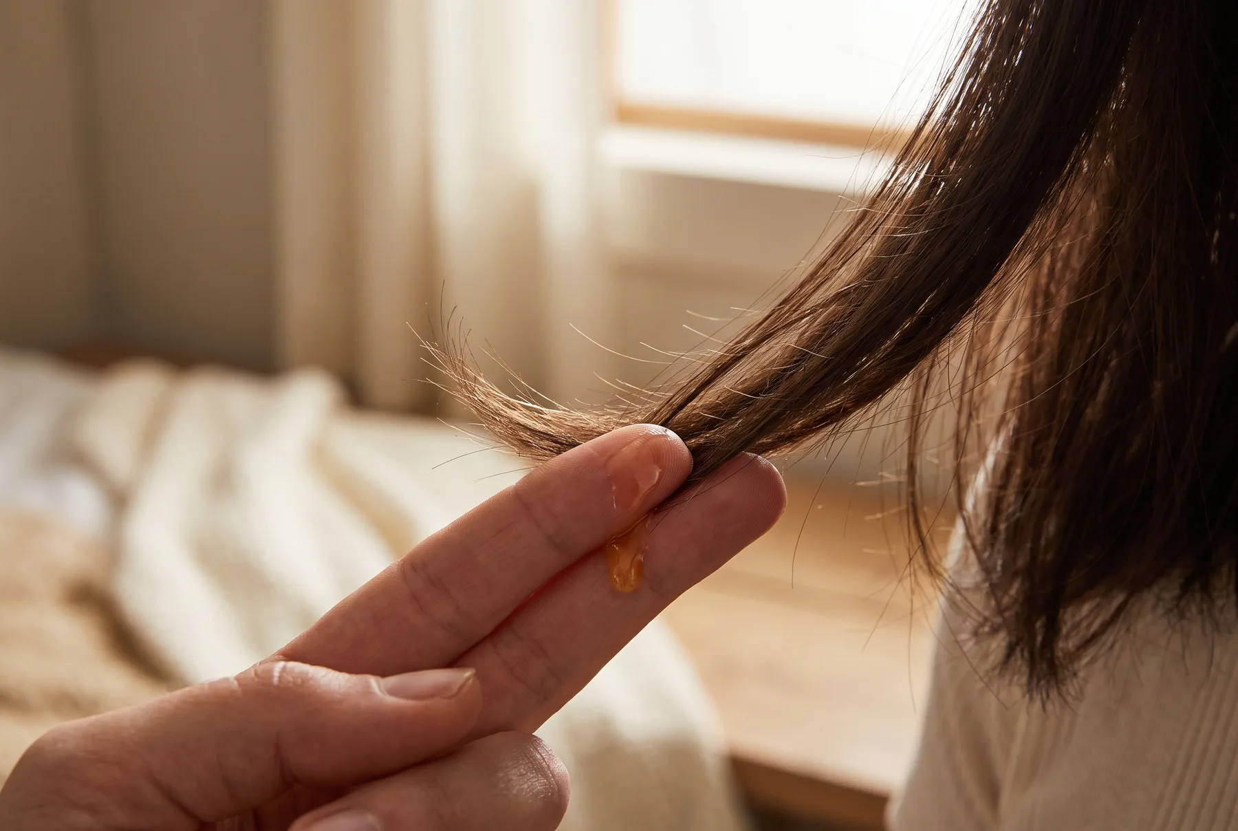 Smoothing a single drop of golden oil through dry hair ends