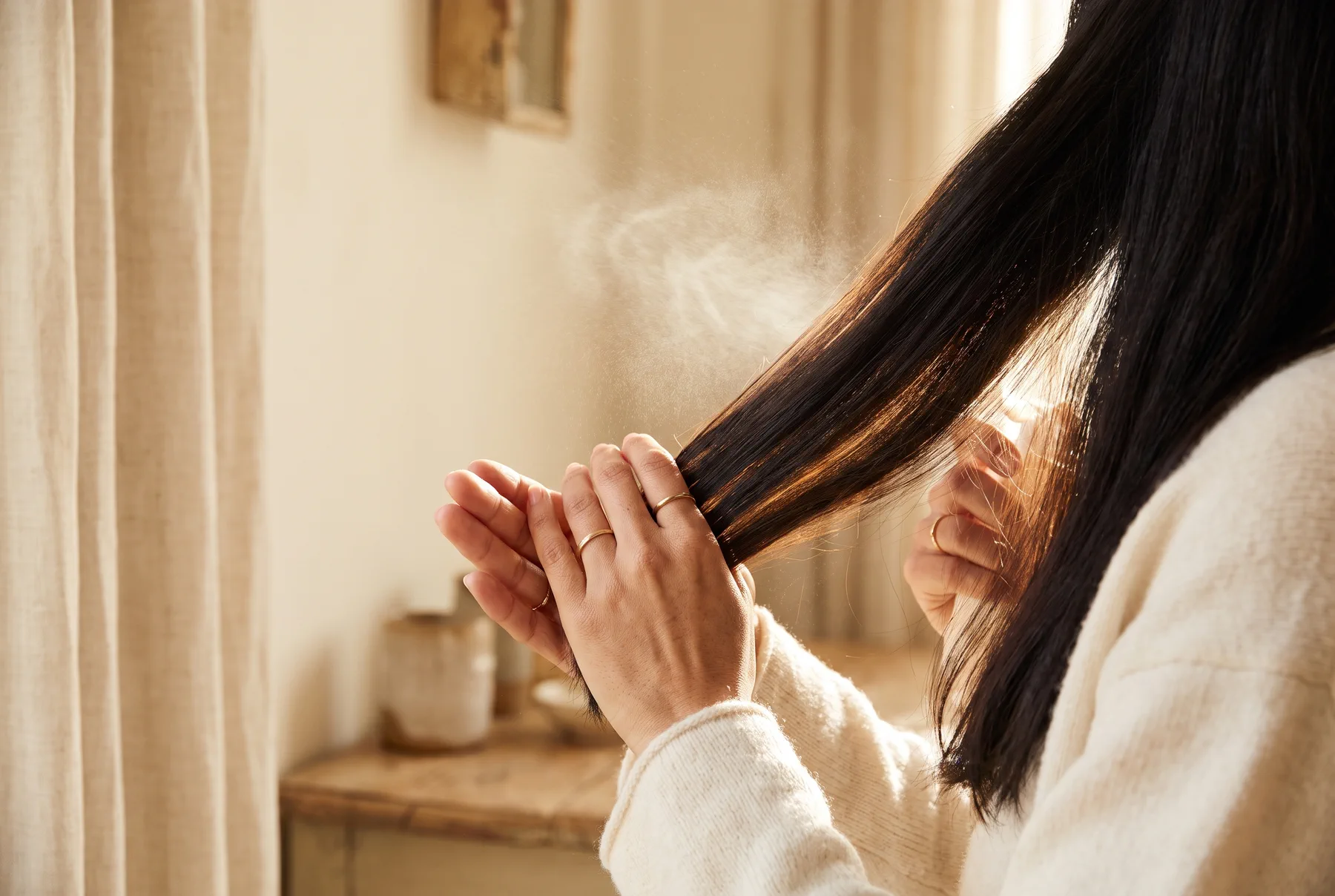 A fine mist drifting through a held-out section of dark hair before styling