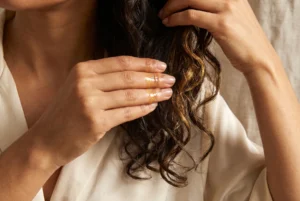 Fingers gliding a small amount of golden oil through mid-lengths and ends, held away from the scalp area